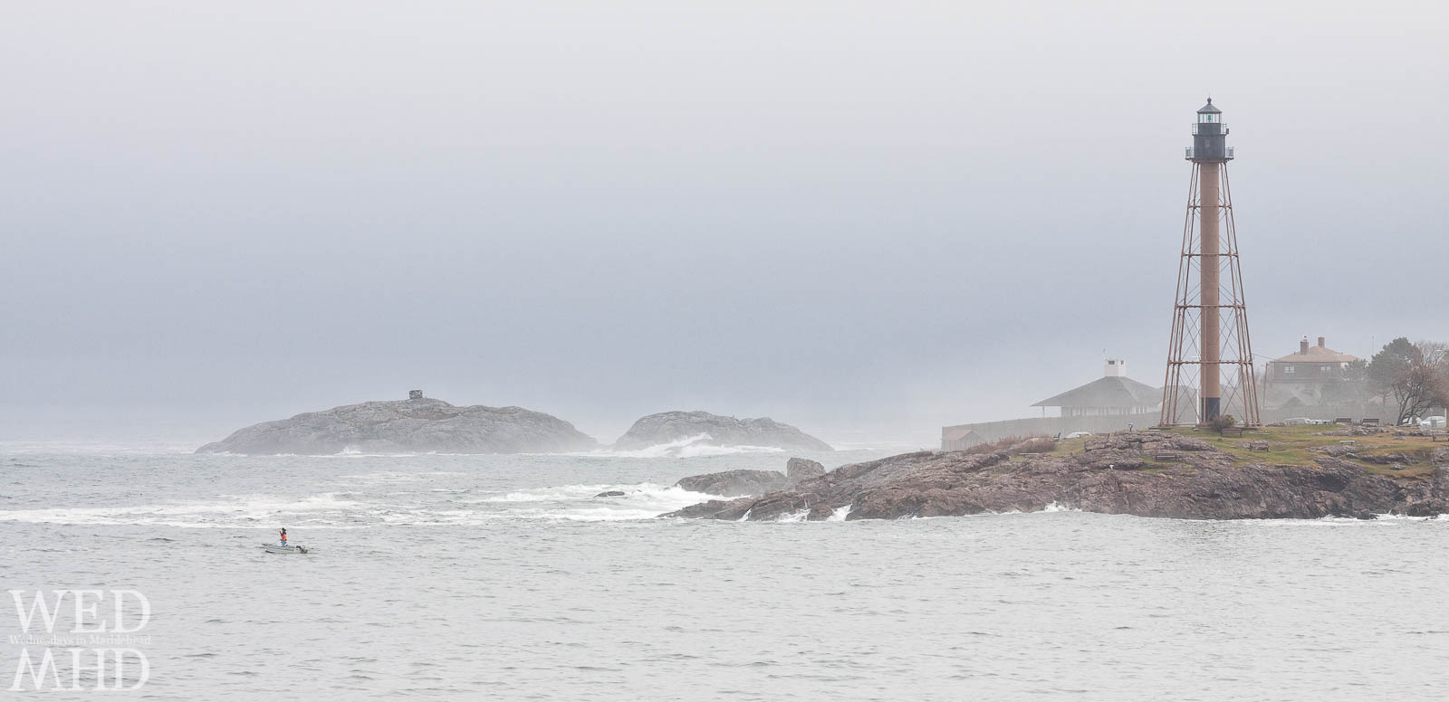 A lone boat at the mouth of Marblehead harbor with someone fishing in the storm