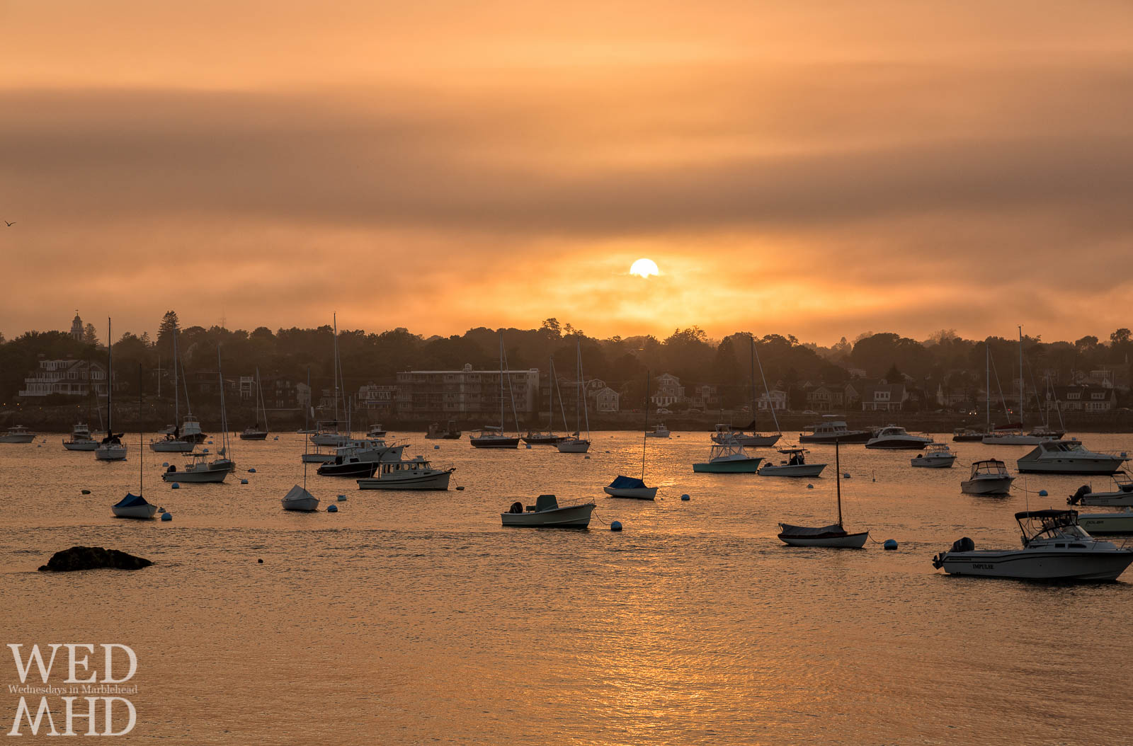 The sun peeks out behind clouds to create a golden sunset on Marblehead Harbor