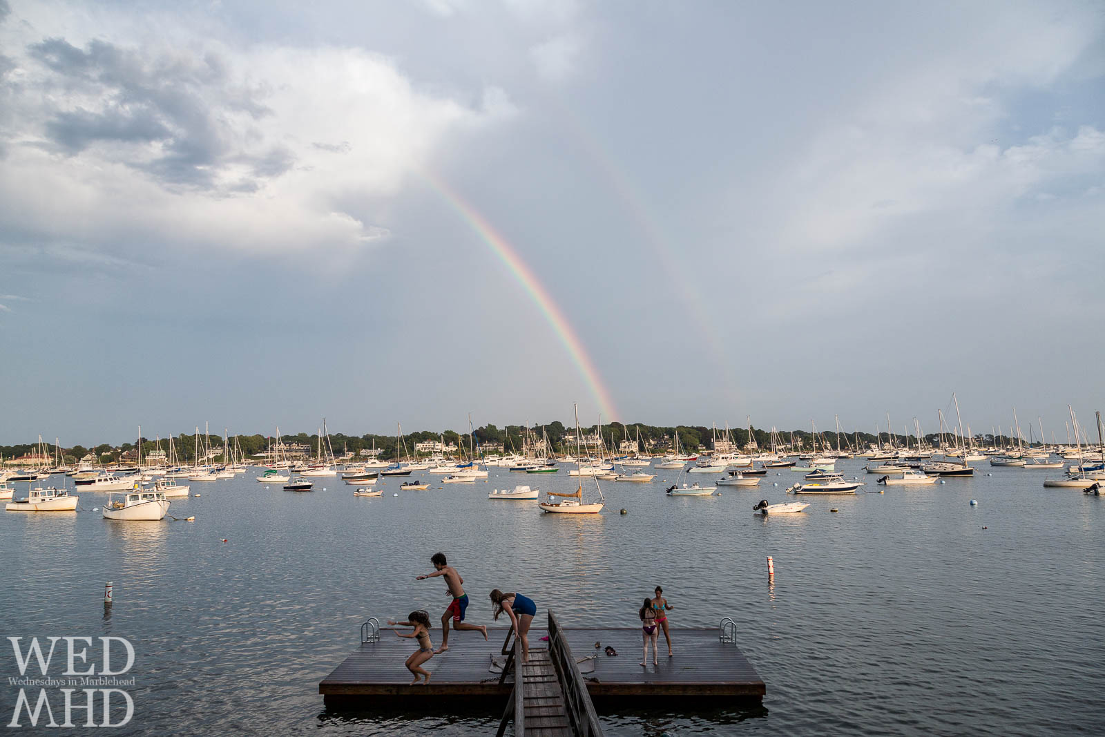 Kids jump off the bridge at Crocker Park with a rainbow visible over Marblehead Harbor