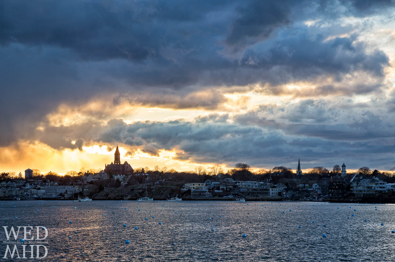 Golden light mixes with dramatic cloud structures over Marblehead's skyline featuring Abbot Hall, St. Michael's and Grace Community Church steeples.