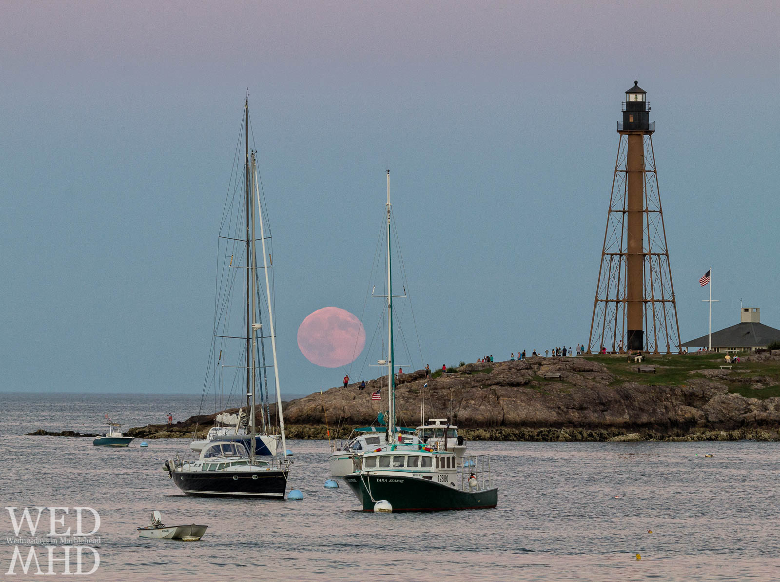 The rare site of a blue moon rising over Chandler Hovey Park is perfectly accented by two blue hulled boats.