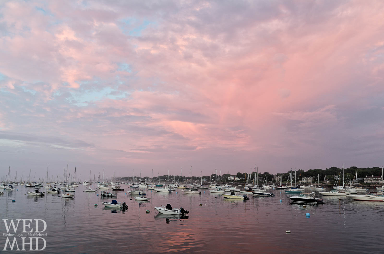 A faint rainbow appears in the sky as a foggy sunset forms over Marblehead Harbor as seen from the Dolphin Yacht Club