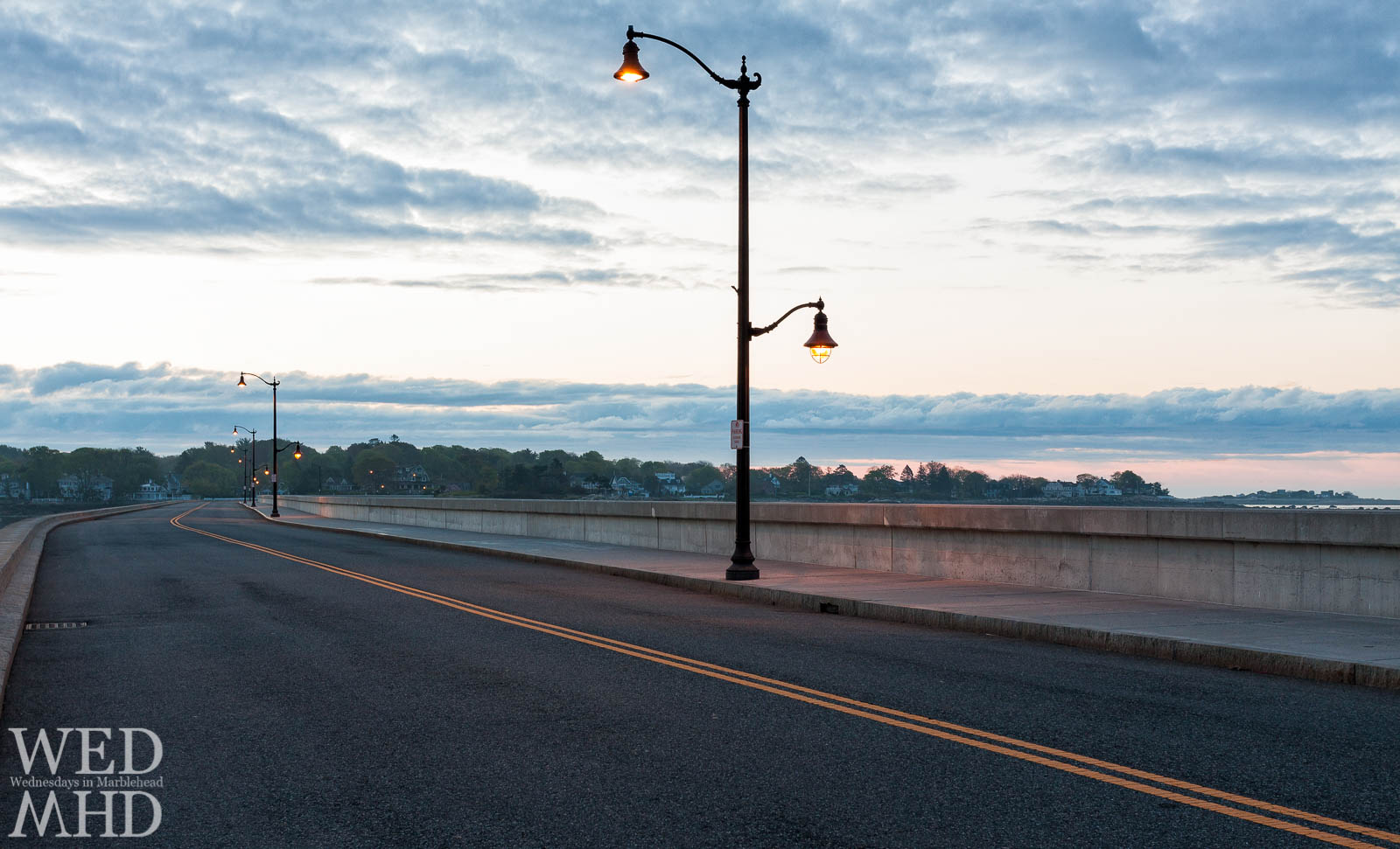 The leading yellow line on the causeway takes the eye past lamp posts lit for the evening