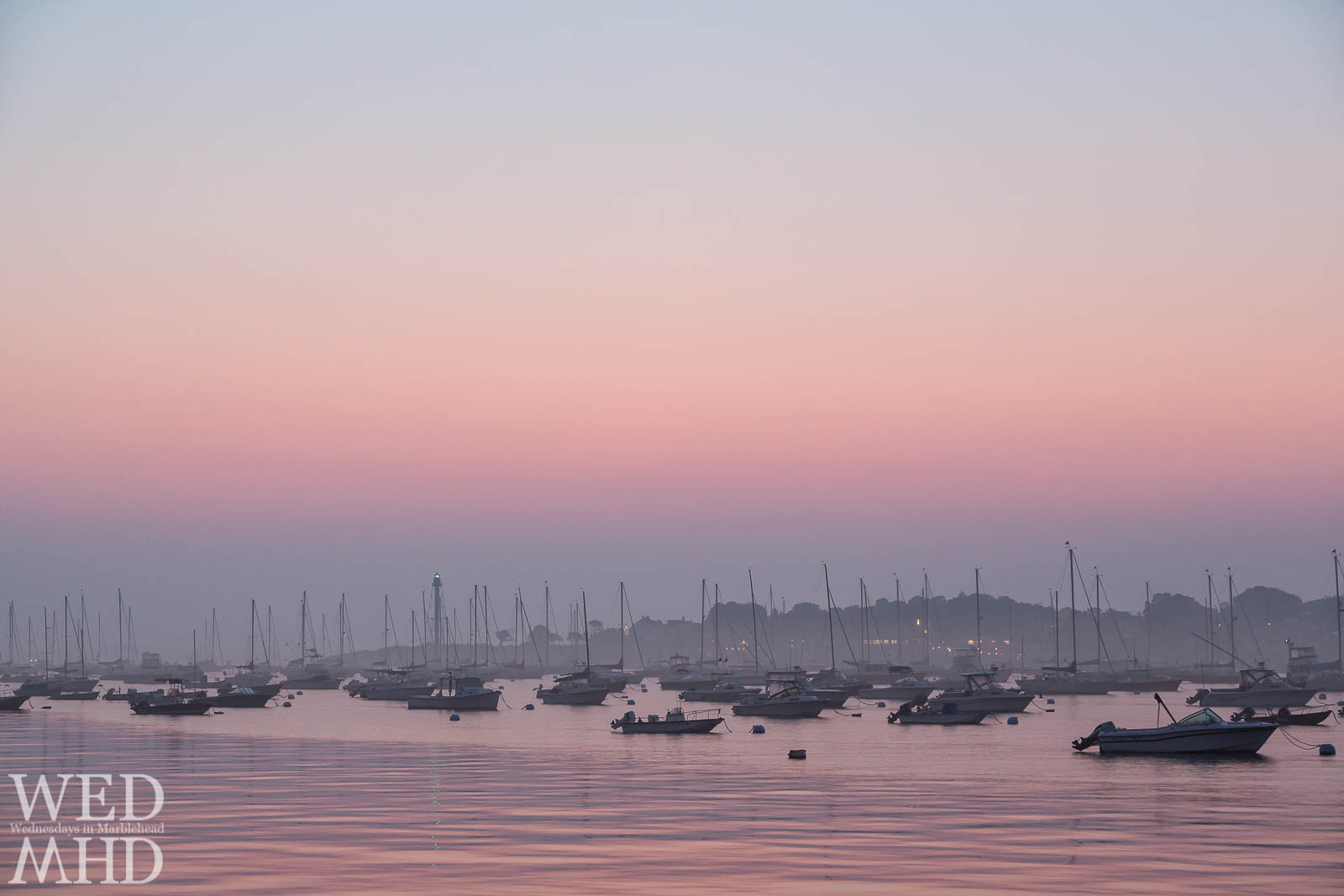 Dawn breaks over Marblehead Harbor casting pink light over the moored boats