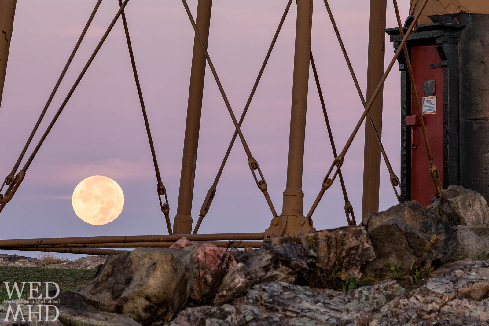 The Hunters Moon rises between supports of Marblehead Light with the red door surrounded by a black frame marking its base