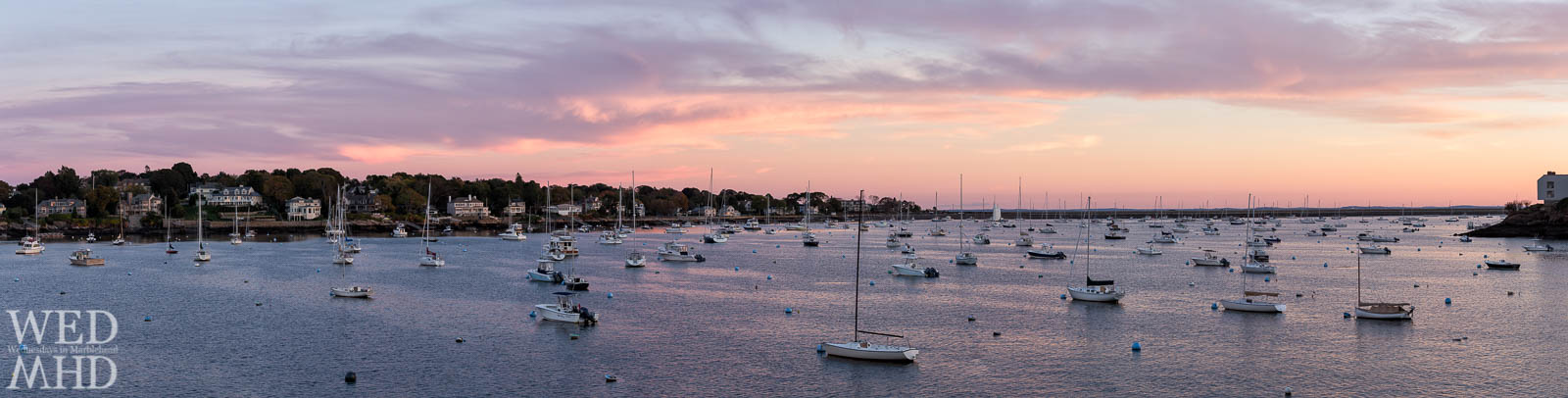 A beautiful sunset forms over inner Marblehead harbor on a mid-October evening with boats still moored and awaiting the last sails of the season