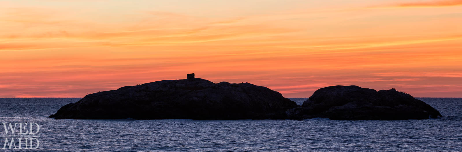 A panoramic view of Marblehead Rock captured under an orange sky at dawn on a mid-October morning