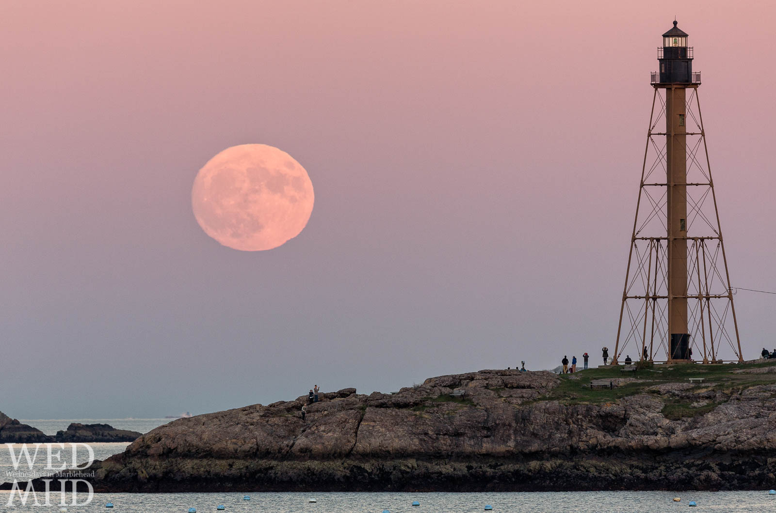 The supermoon rises over Marblehead Light as the largest full moon in over 60 years. Crowds gather at Chandler Hovey Park to watch the display.