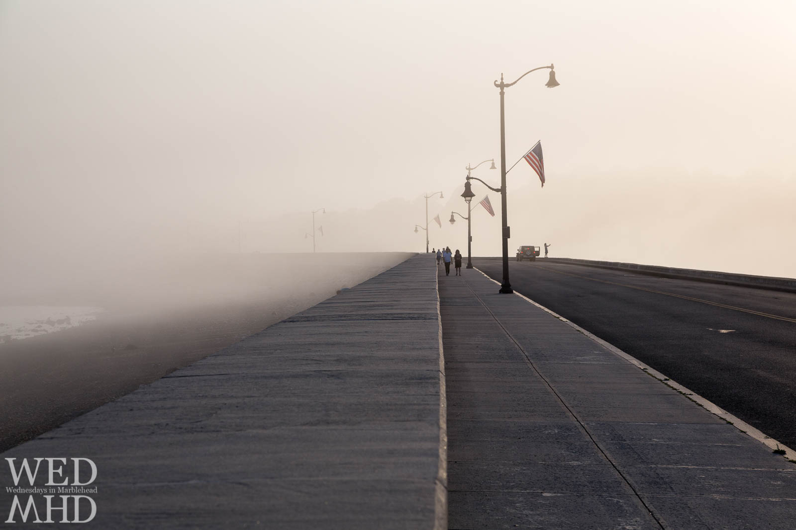 A driver pulls over on the causeway to take a photo of a July sunset mixed with fog over Marblehead harbor thus capturing the moment forever