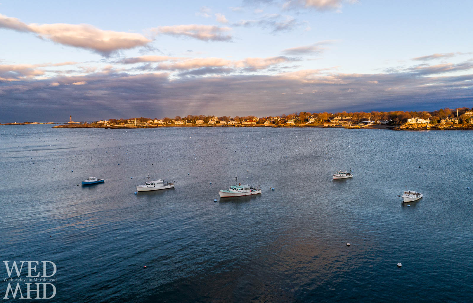 The working boats in Marblehead Harbor are backed by the golden light of sunset reflecting off Marblehead Neck