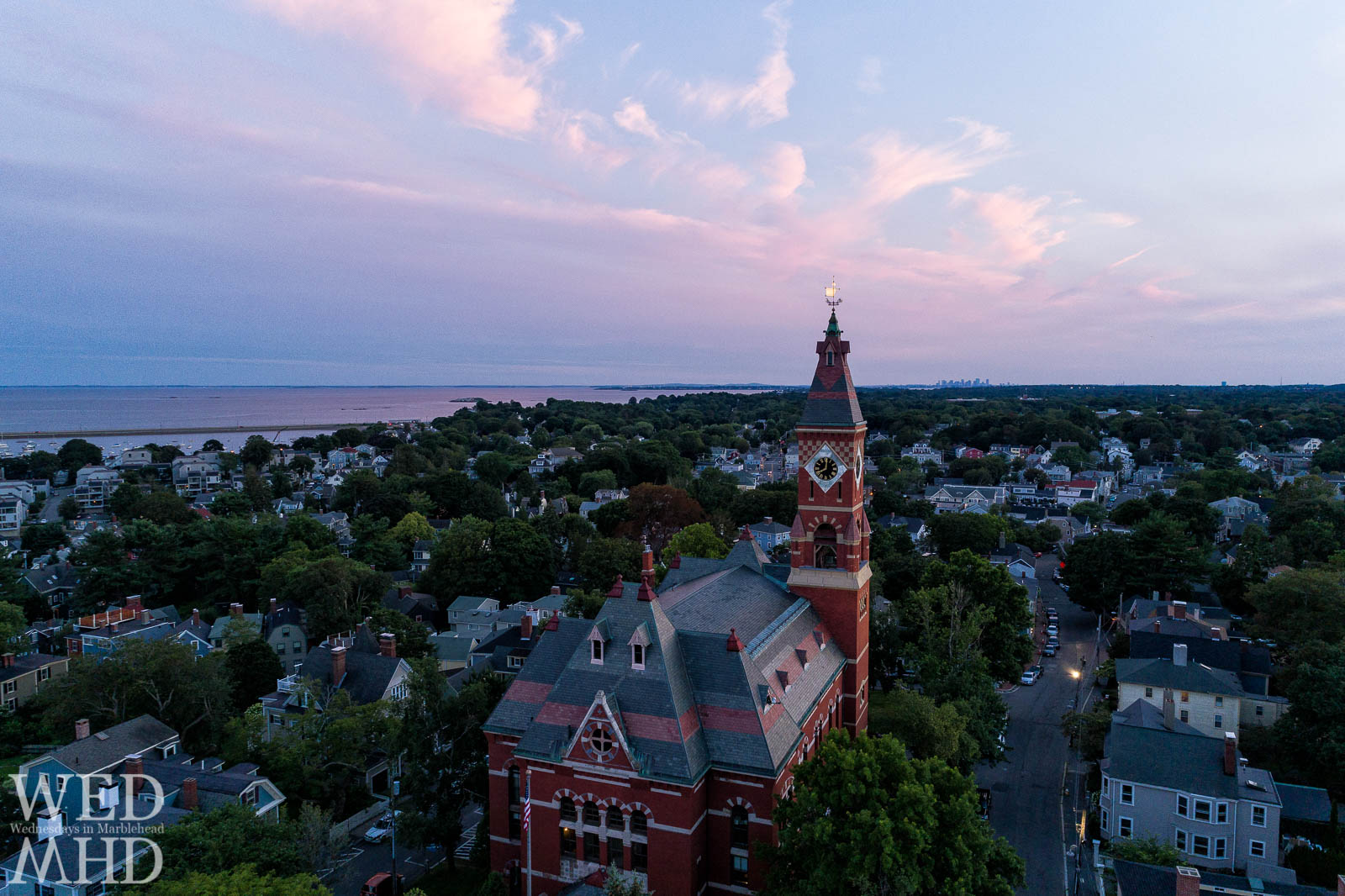 The sun sets casting a pink hue in the sky and a last light on Abbot Hall breaking through the horizon along Washington Street