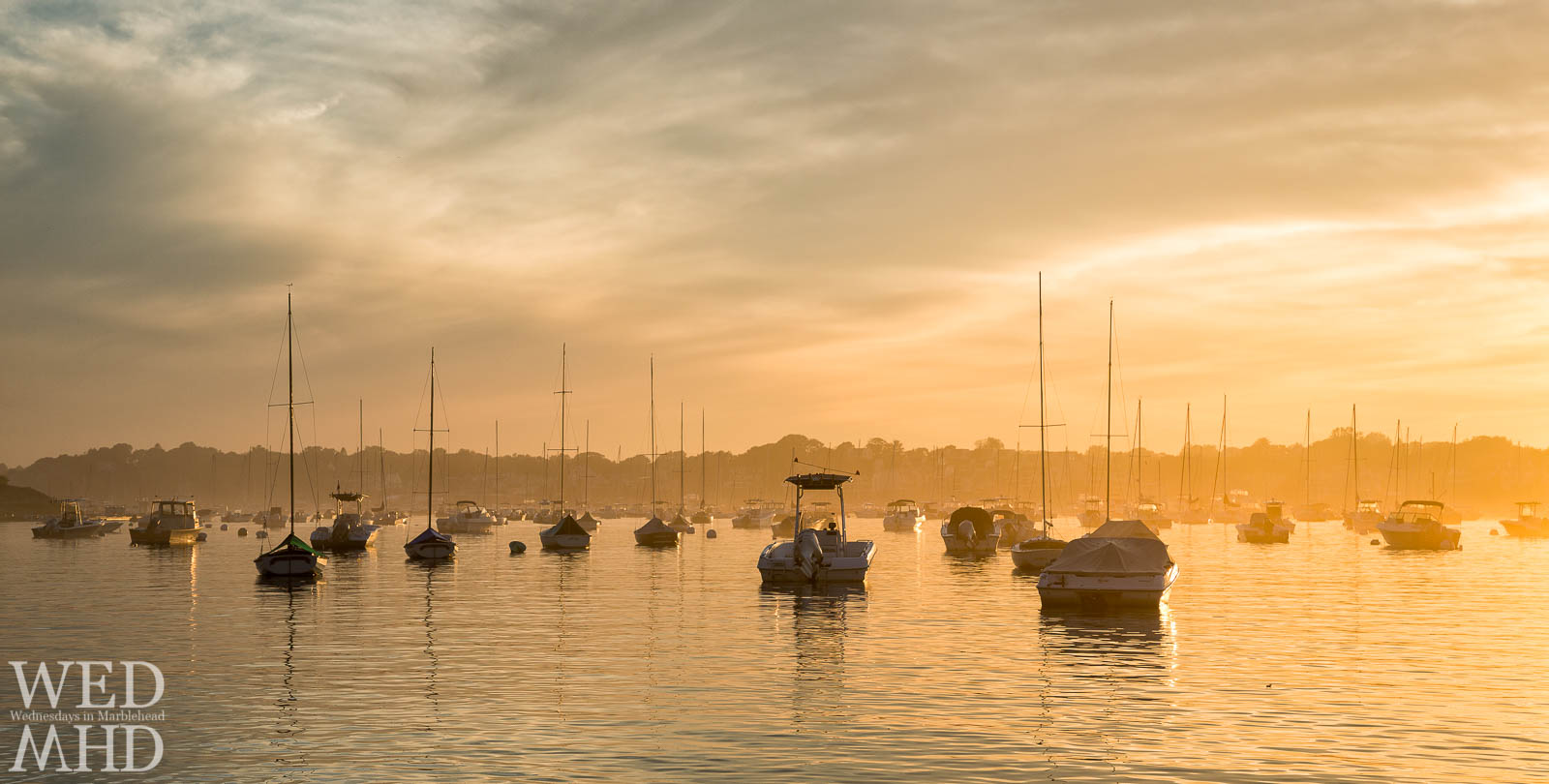 Boats moored in Marblehead seem to float on a golden harbor as the sunset is diffused by evening fog to create a beautiful scene