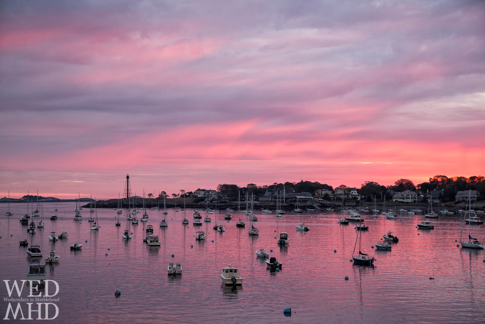An incredible mix of pinks and purples lights up the sky on a Marblehead Harbor dawn with boats in the harbor all pointing toward Marblehead Light