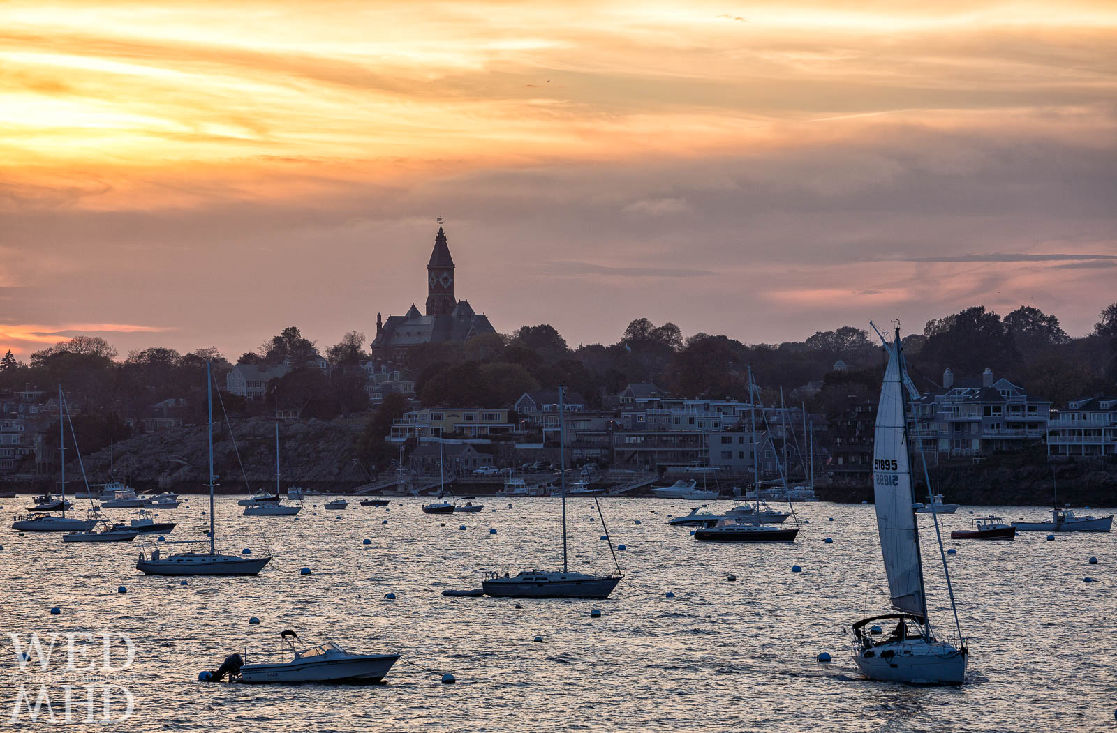 A lone boat heads out at sunset for one last sail in October with Abbot Hall and a few boats setting the backdrop