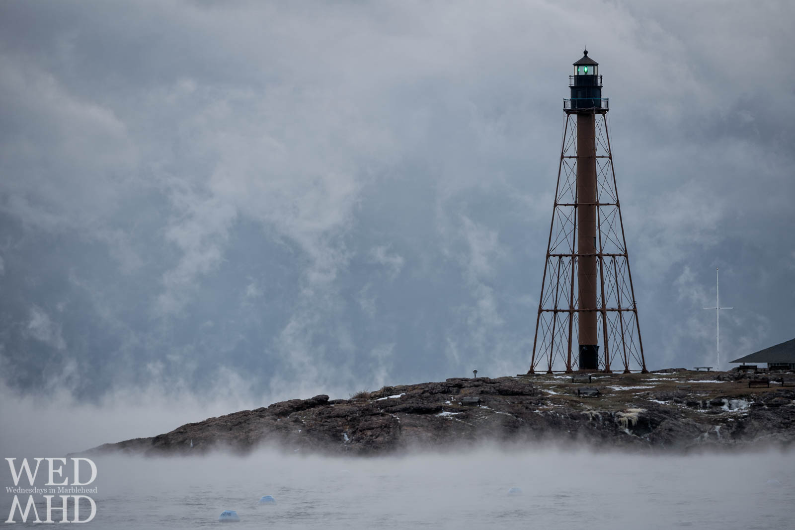 Marblehead Light shines its green beacon in the smoke on an arctic morning