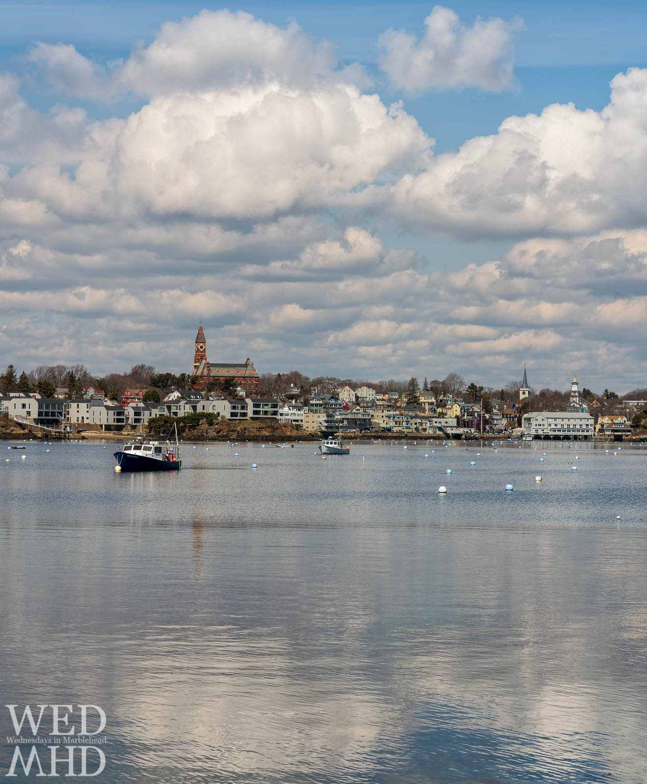 Clouds build and reflect in the still waters of Marblehead Harbor at Noon on an mid-April day