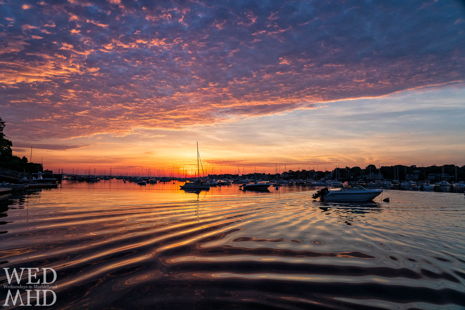A passing boat's wake creates subtle waves to accentuate sunrise reflections on Marblehead Harbor