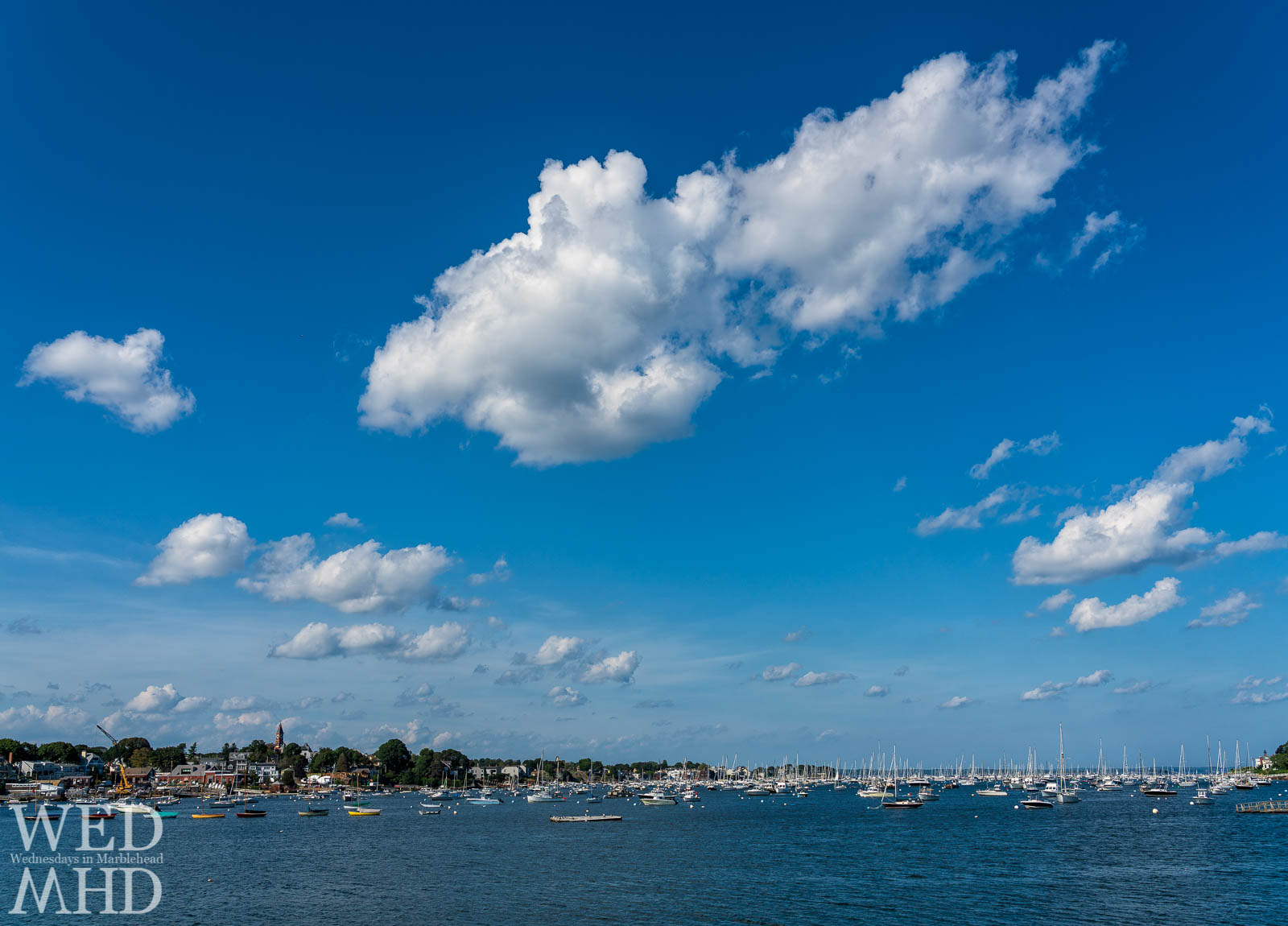 Blue sky punctuated by white clouds rise over Marblehead Harbor on a hot summer day