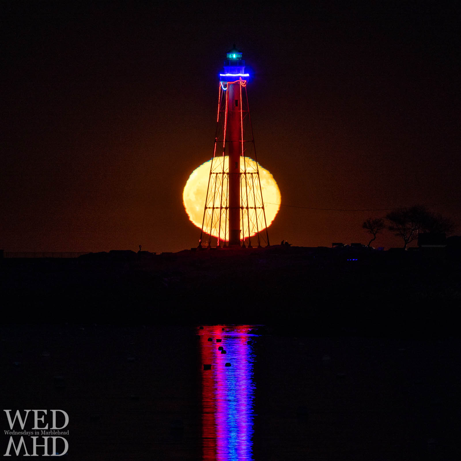 The full cold moon crosses behind Marblehead Light on a late evening in December