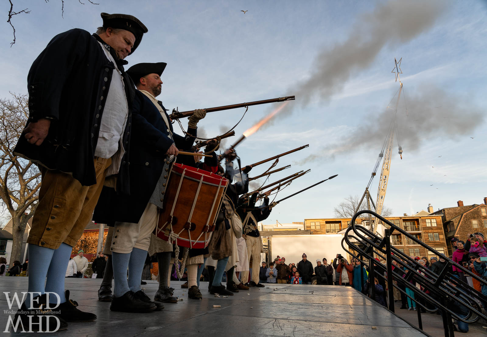 Glover's Regiment fires a volley with the star overhead framed by smoke and a crowd gathered to watch the subsequent crossing of the Marblehead harbor