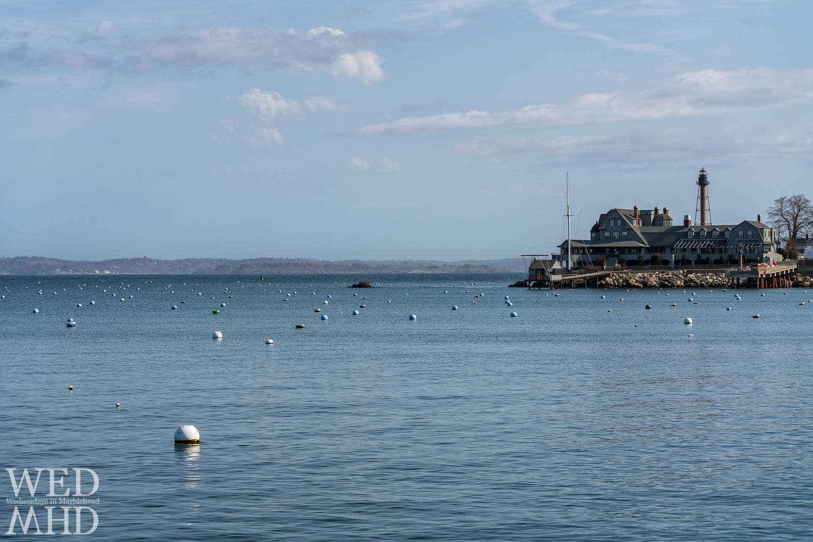 Empty moorings dot the waters in front of the Corinthian Yacht Club with Marblehead Light standing tall behind it