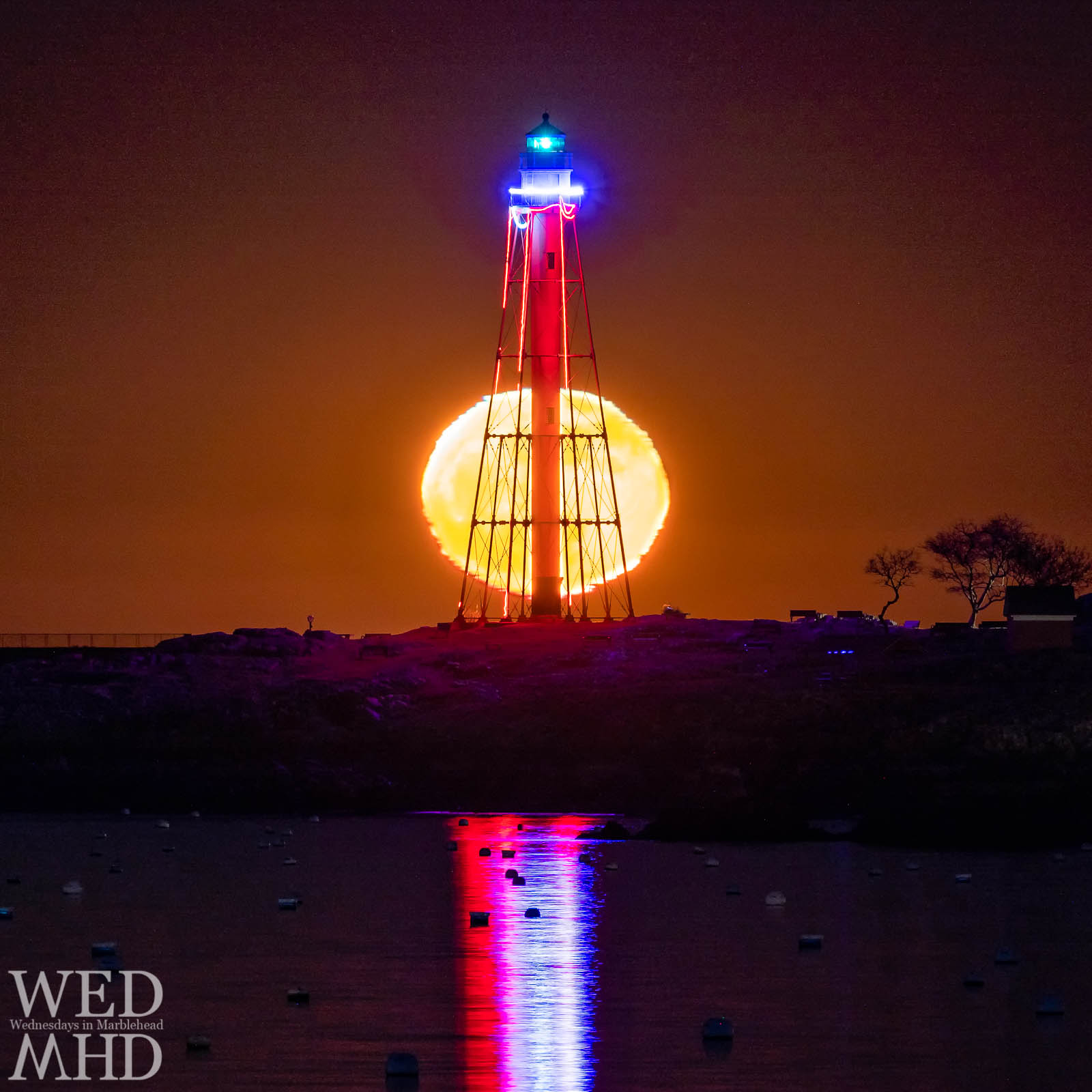 Marblehead light is backlit by moonglow in this long exposure image that captures the reflection of red, white and blue lights in the water below