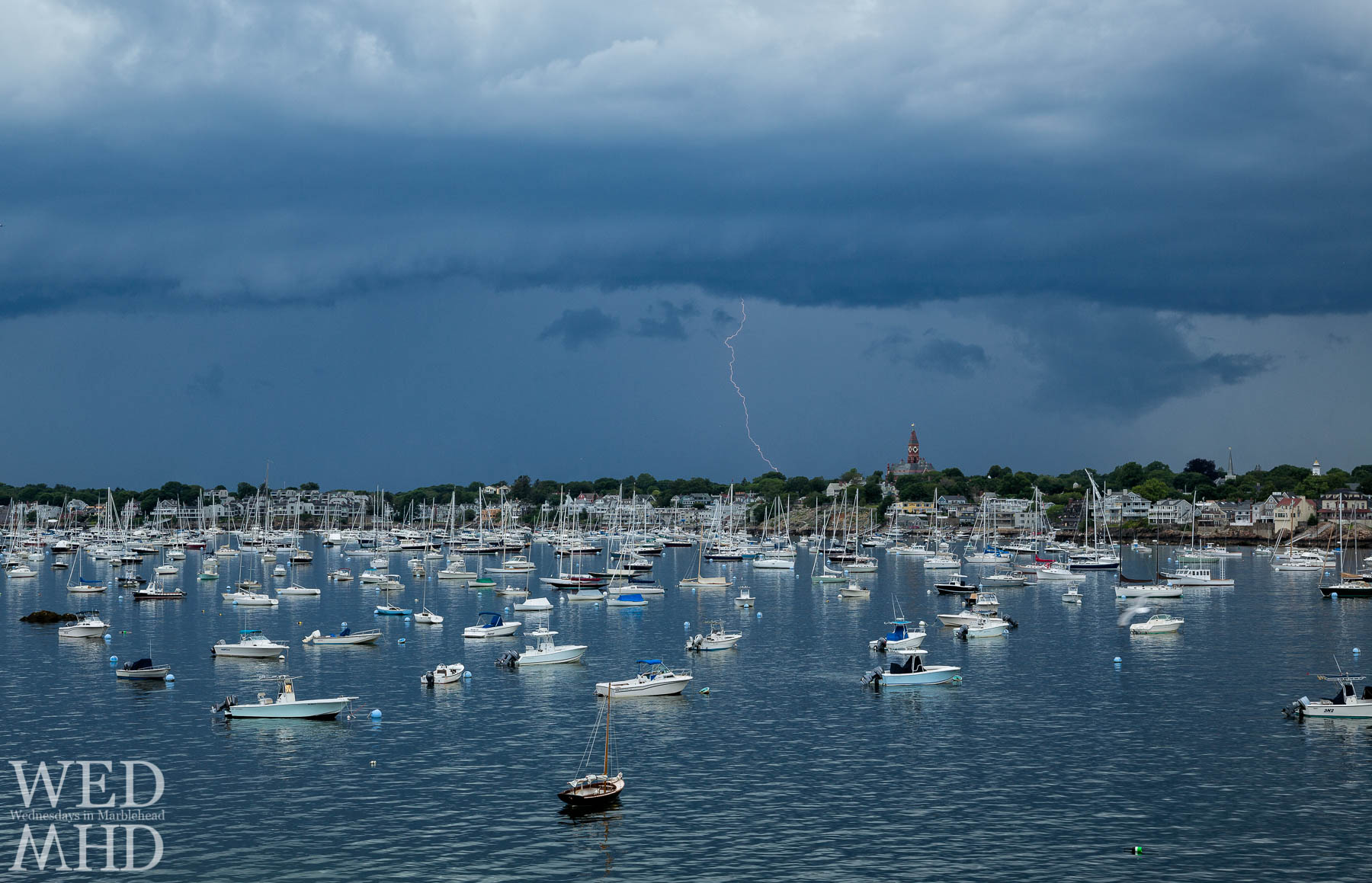 A June storm fires off a lightning bolt behind Abbot Hall with boats filling Marblehead harbor
