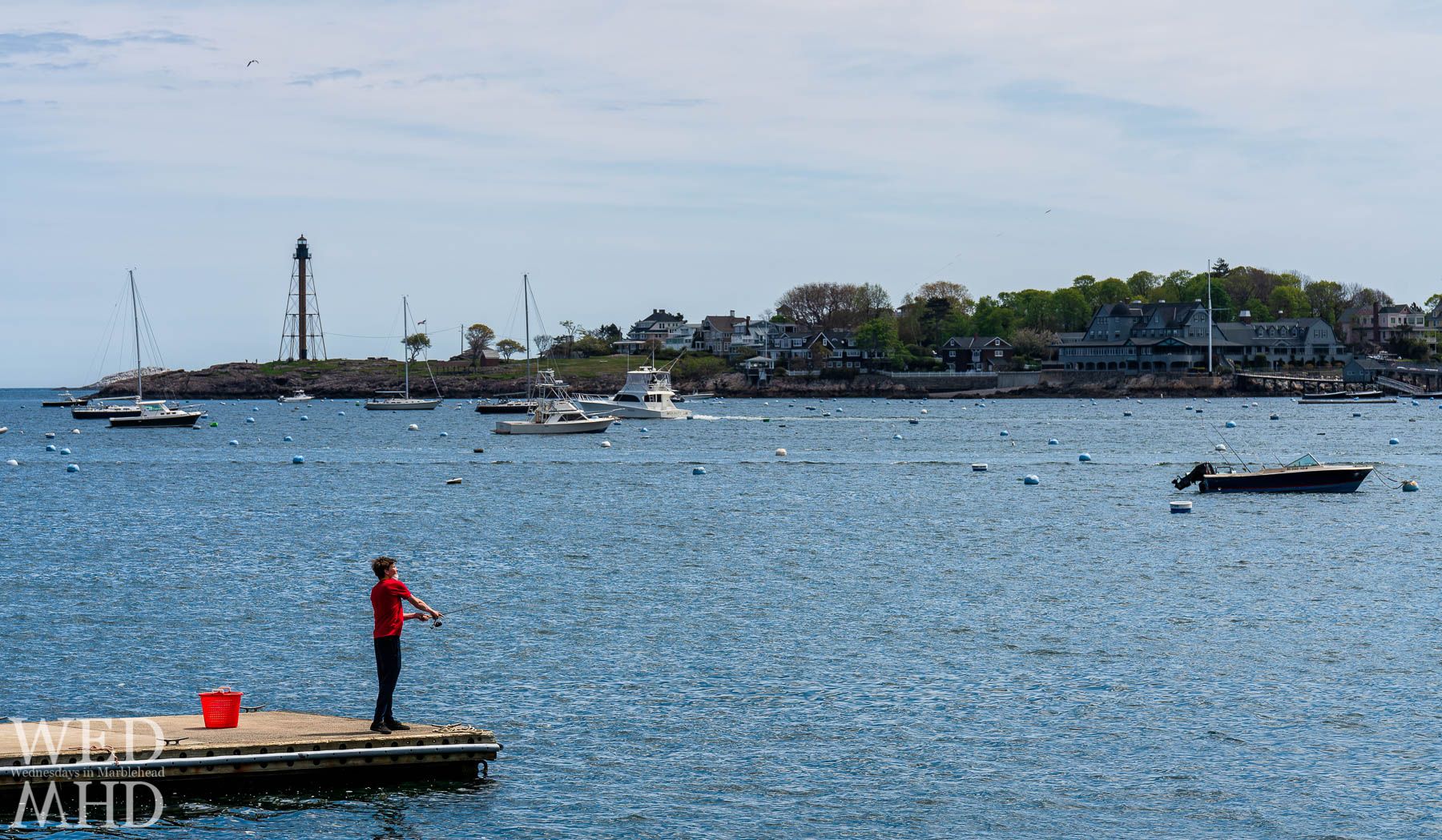 A young man wears a mask while fishing off of the State Street Landing in Marblehead