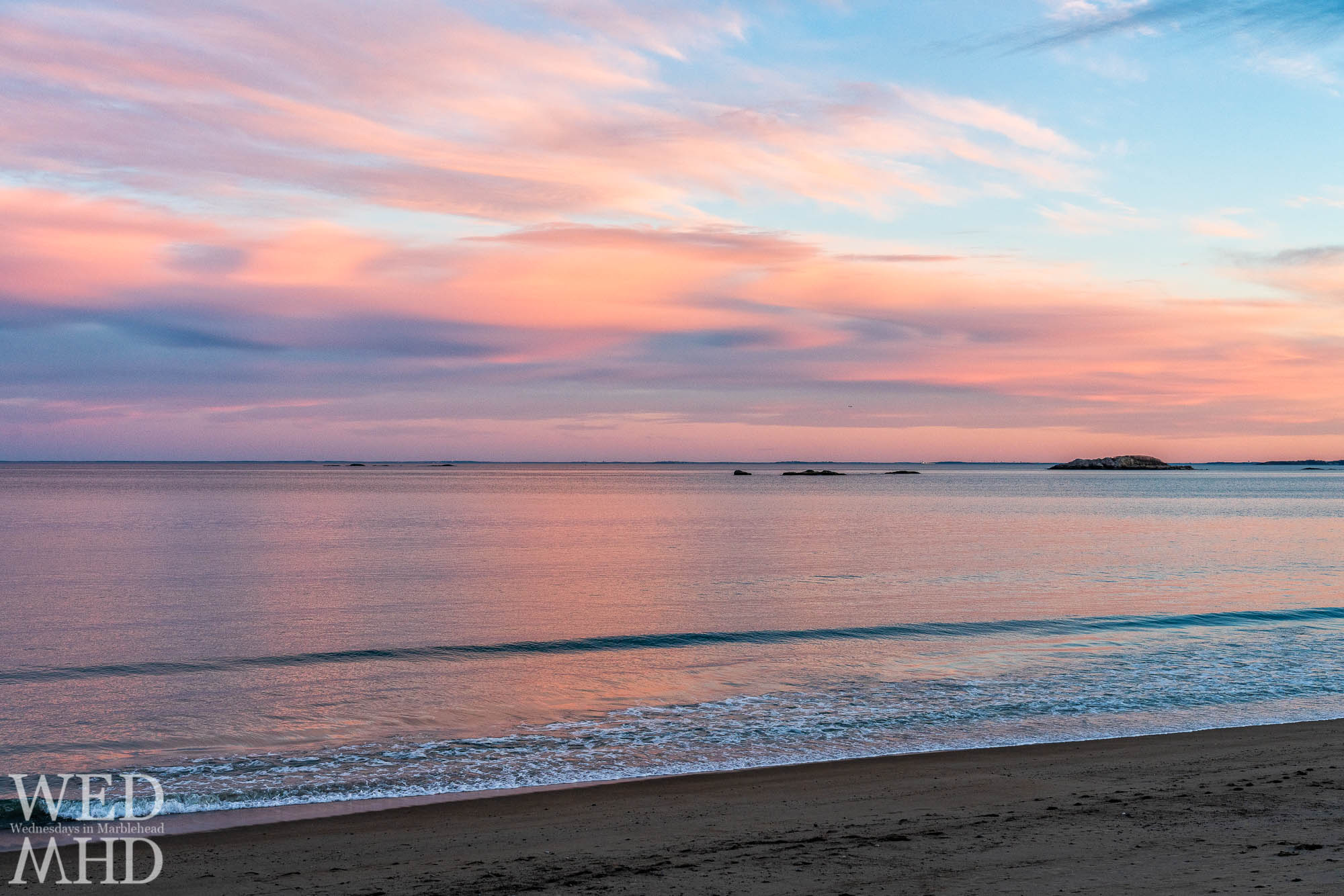A calm ocean reflects the light of sunset on a spring evening with Ram Island jutting out in the distance