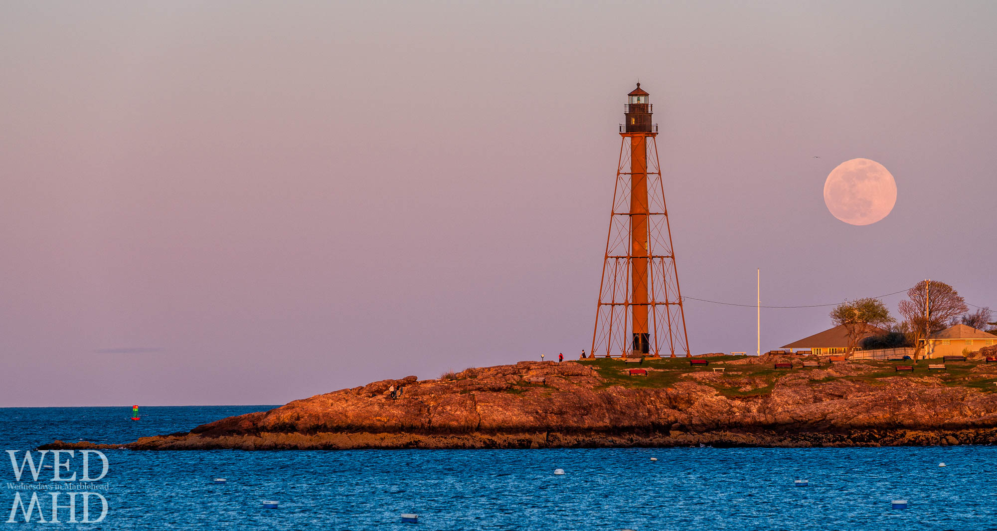 The full pink moon rises beside Marblehead Light with a channel marker caught reflecting the light of the setting sun