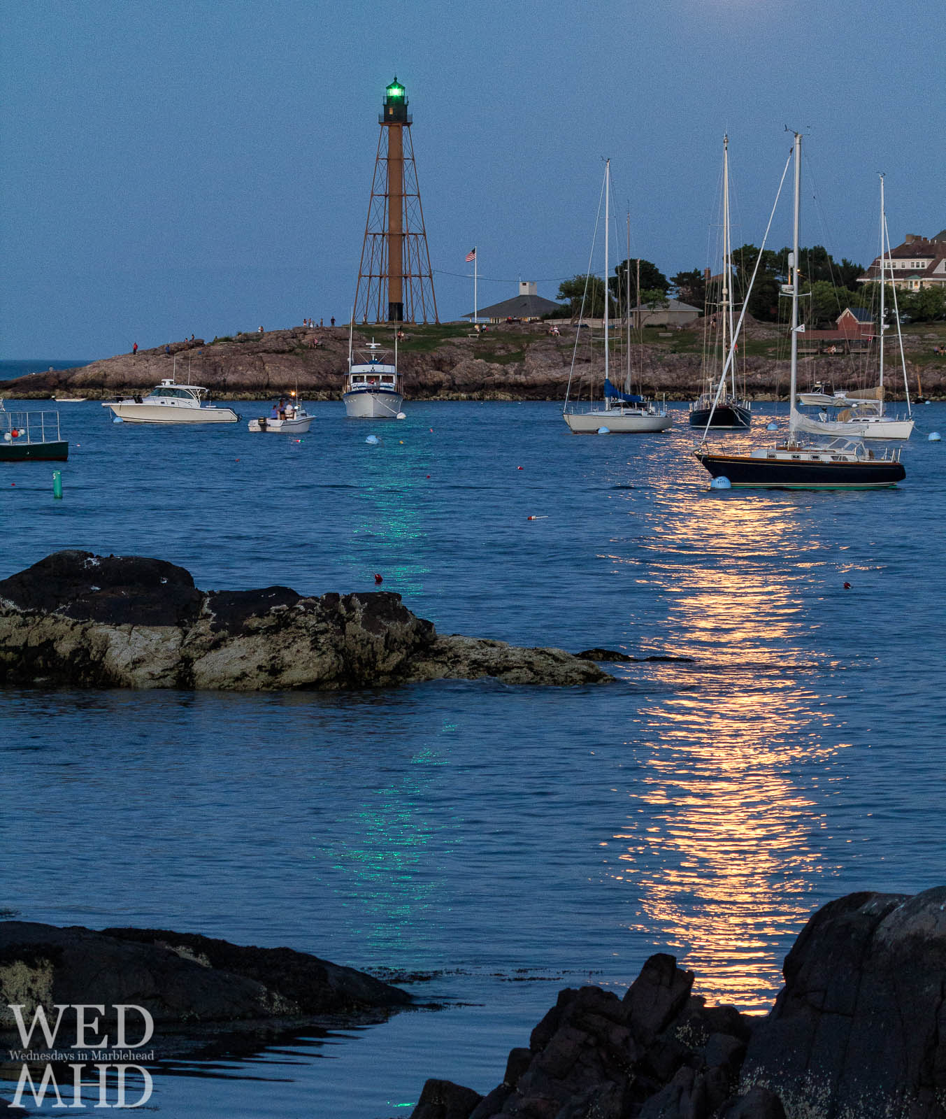 The golden glow from a risen moon casts its light alongside the green of Marblehead Light
