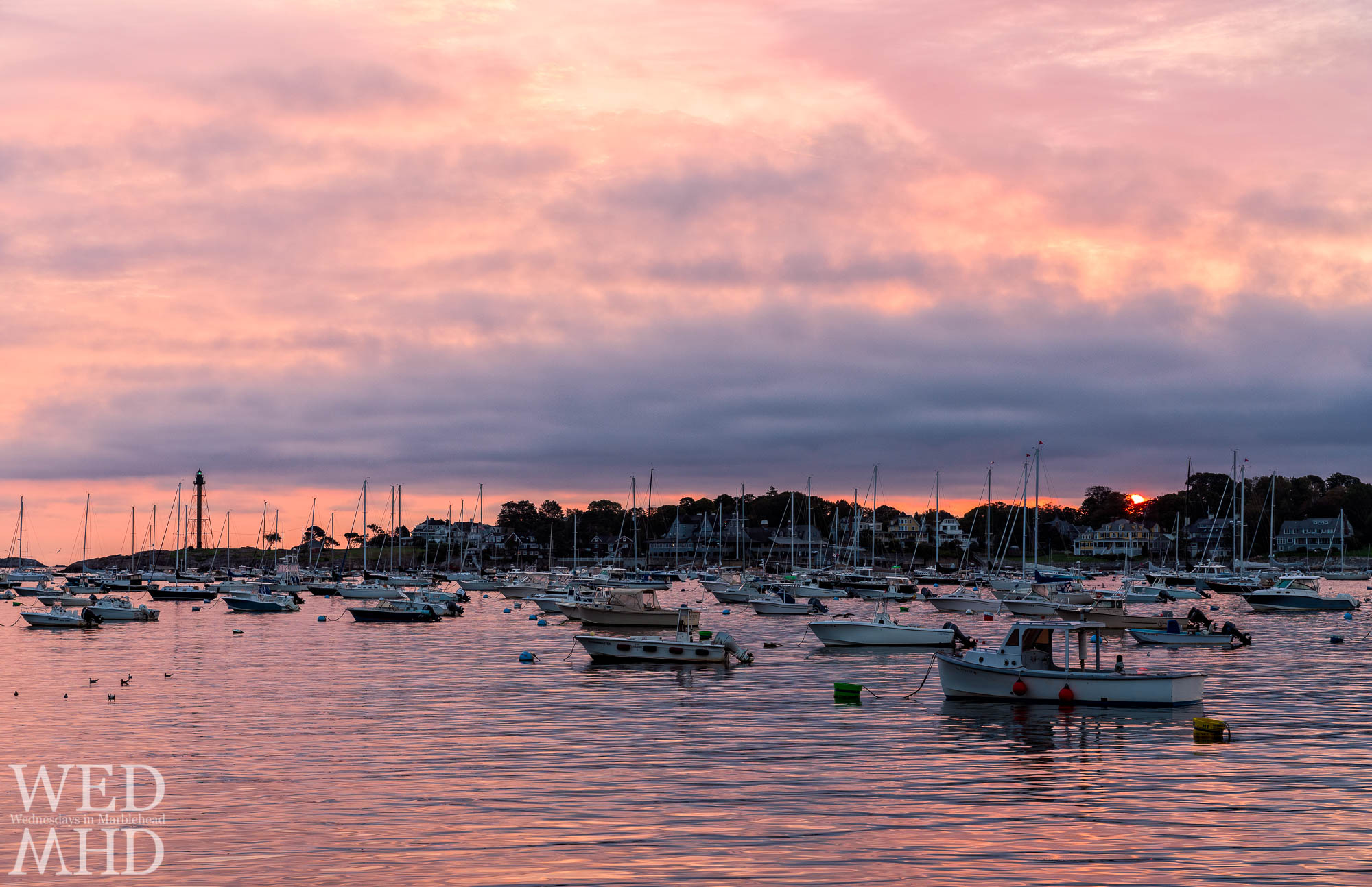 The rising sun is captured behind Marblehead Neck in this view from Tuckers Wharf at dawn