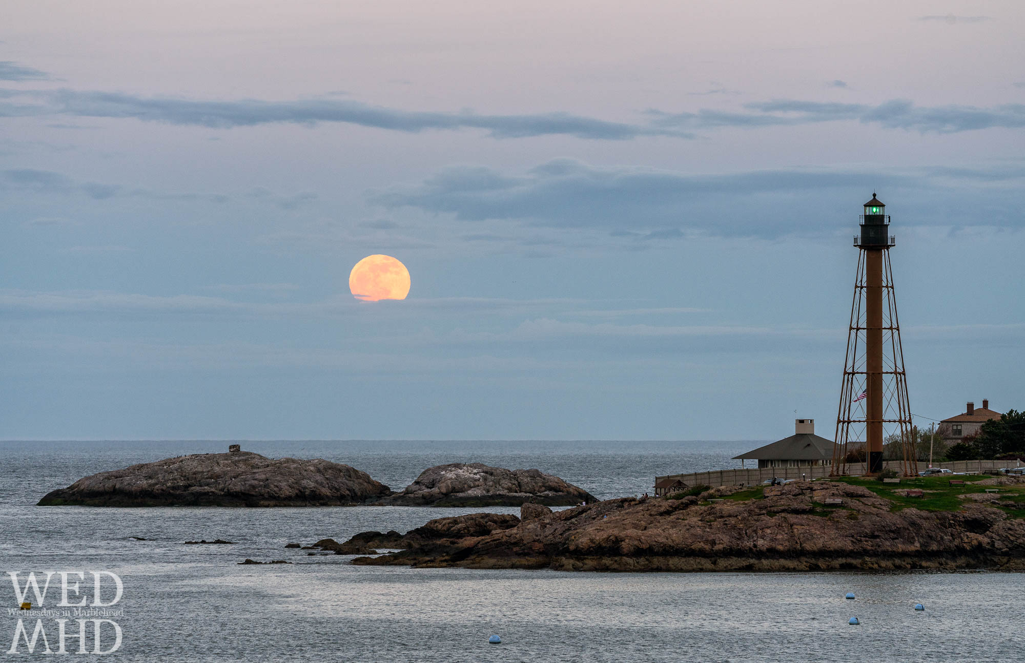 The full moon rises above the clouds at Chandler Hovey Park with Marblehead Light standing tall